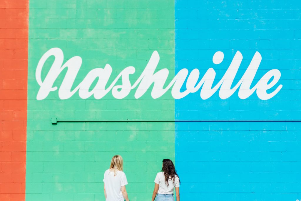 Humans near multi-colored Nashville sign.